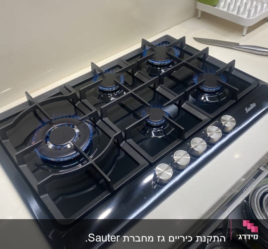 כיריים גז עם חמש להבות דולקות וכפתורי שליטה כסופים